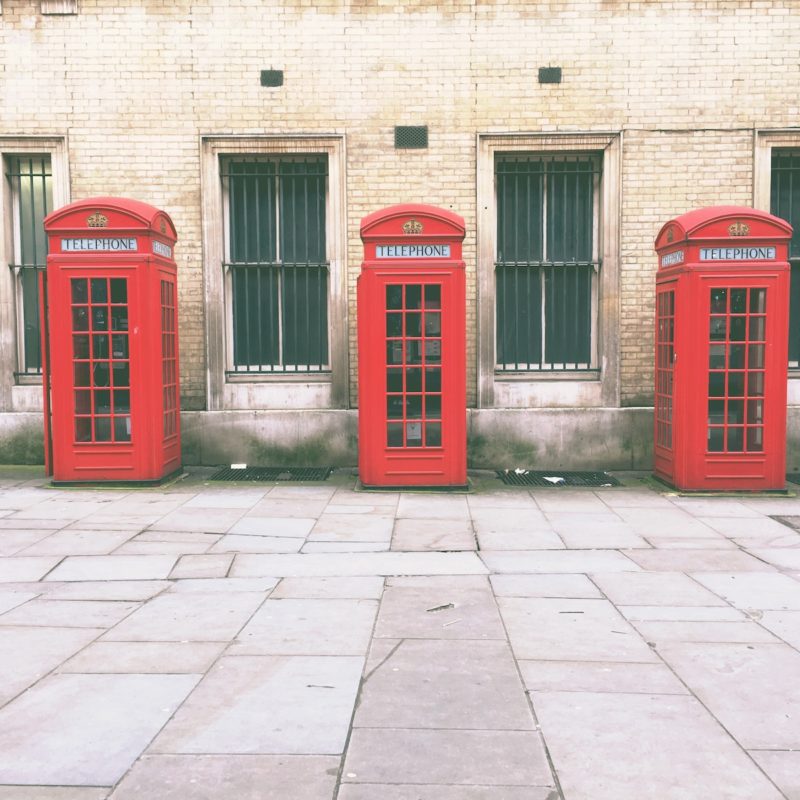 red telephone booth beside brown concrete building